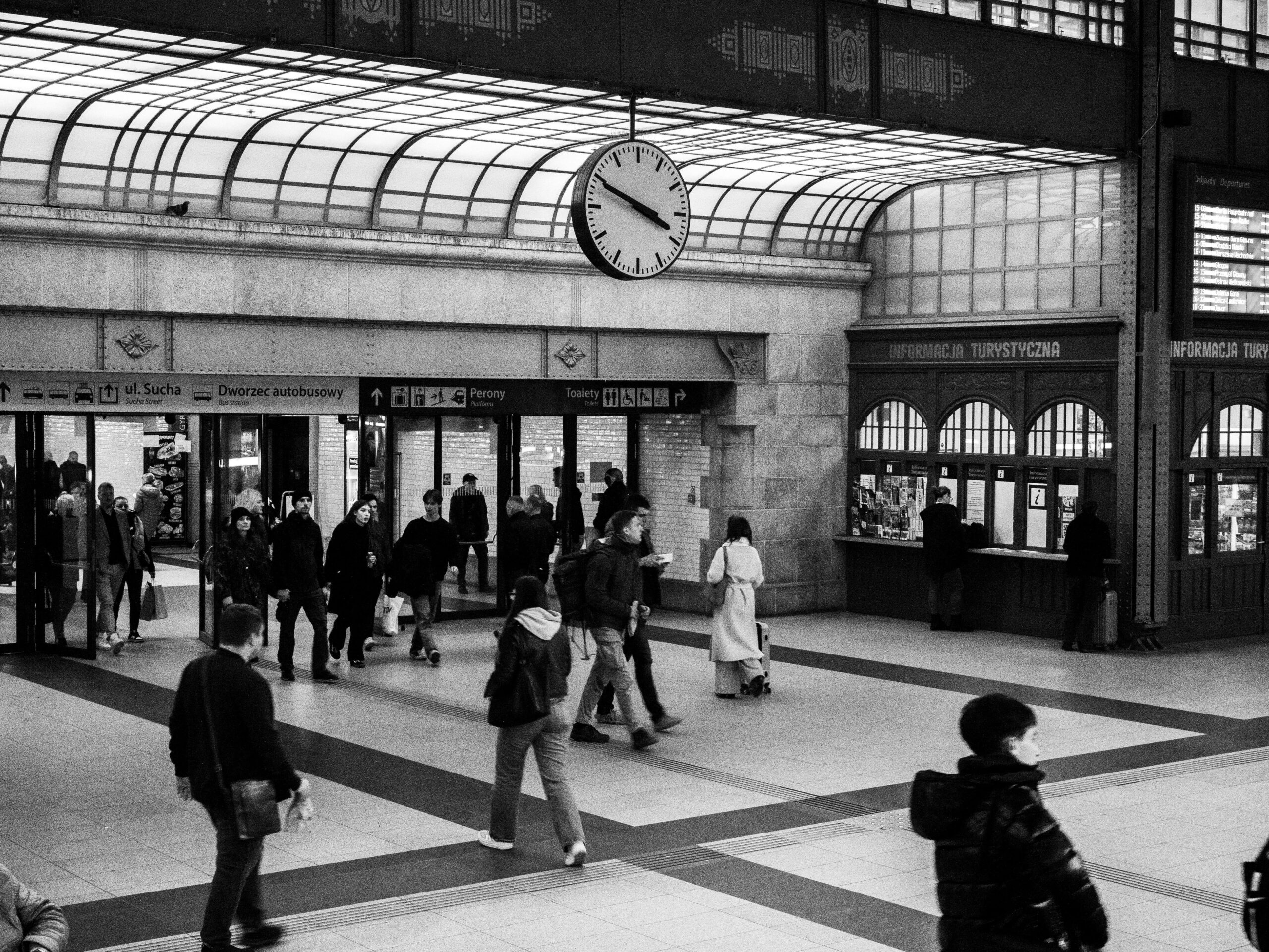 Monochrome Ansicht eines &uuml;berf&uuml;llten Bahnhofs mit einer markanten Uhr und Fahrkartenschaltern.