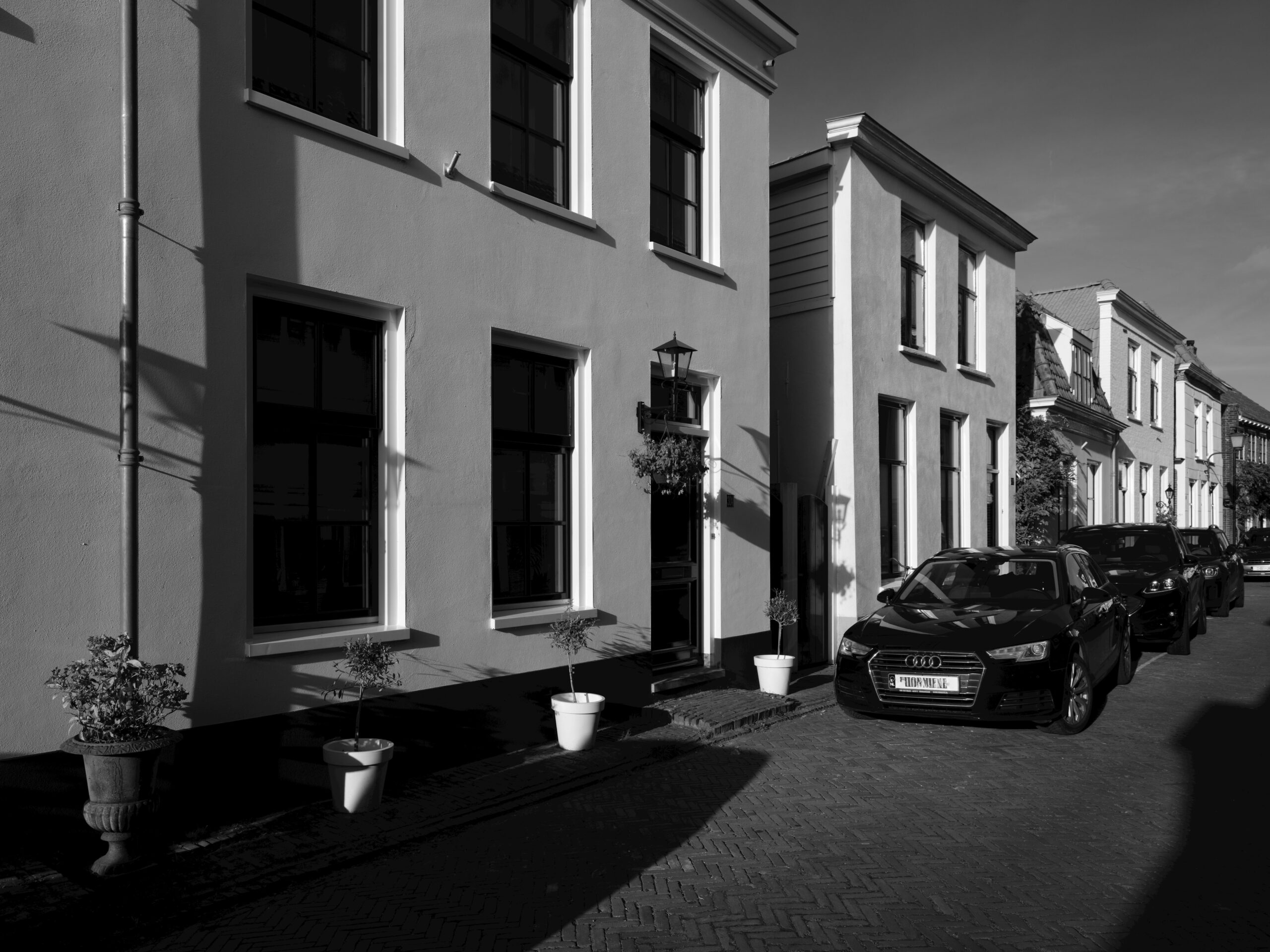 Ein Schwarzwei&szlig;foto von charmanten H&auml;usern mit geparkten Autos in einer sonnenbeschienenen Stra&szlig;e.
