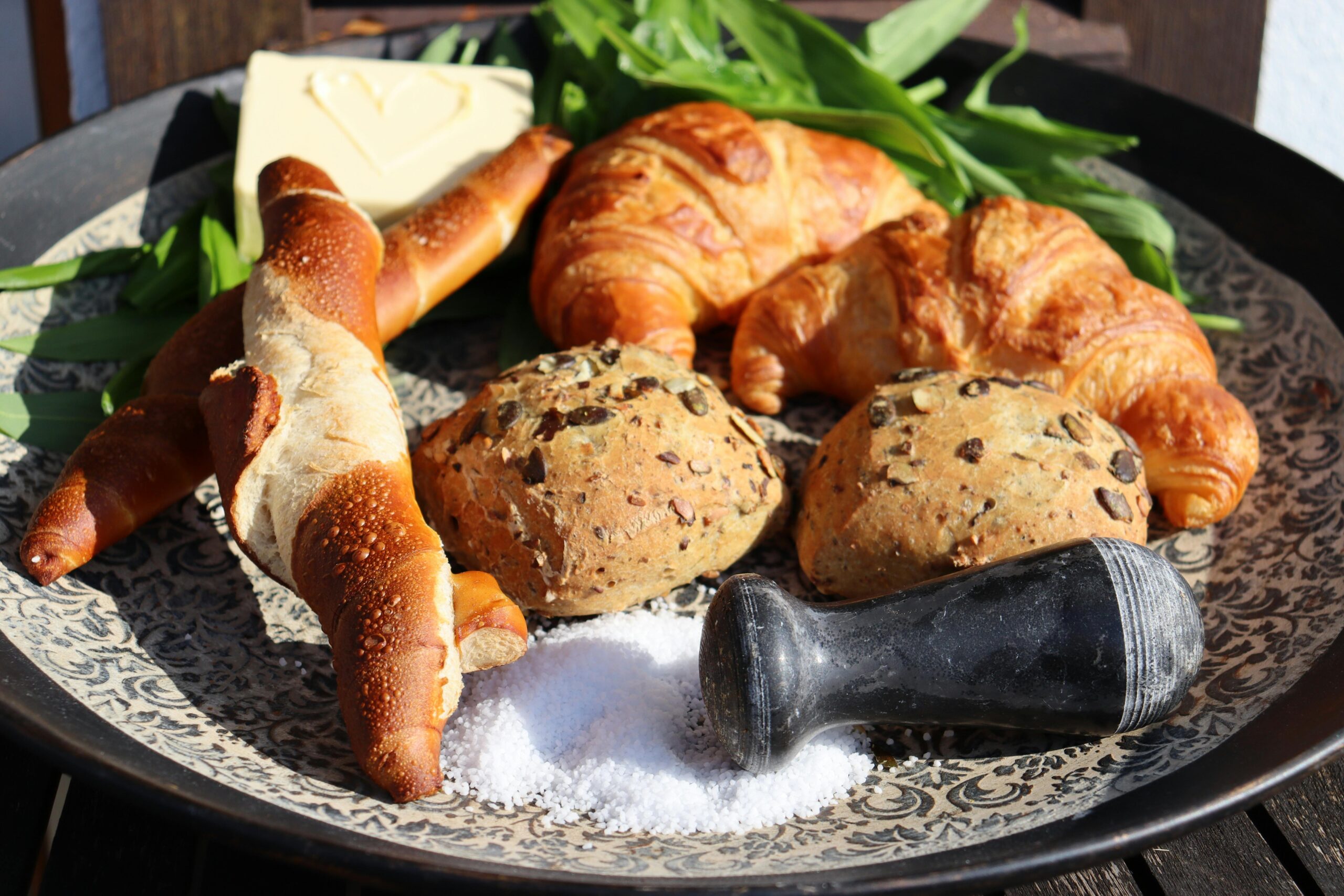 Eine Auswahl an frischem Brot, darunter Croissants und Brezeln, serviert mit Butter und Salz.