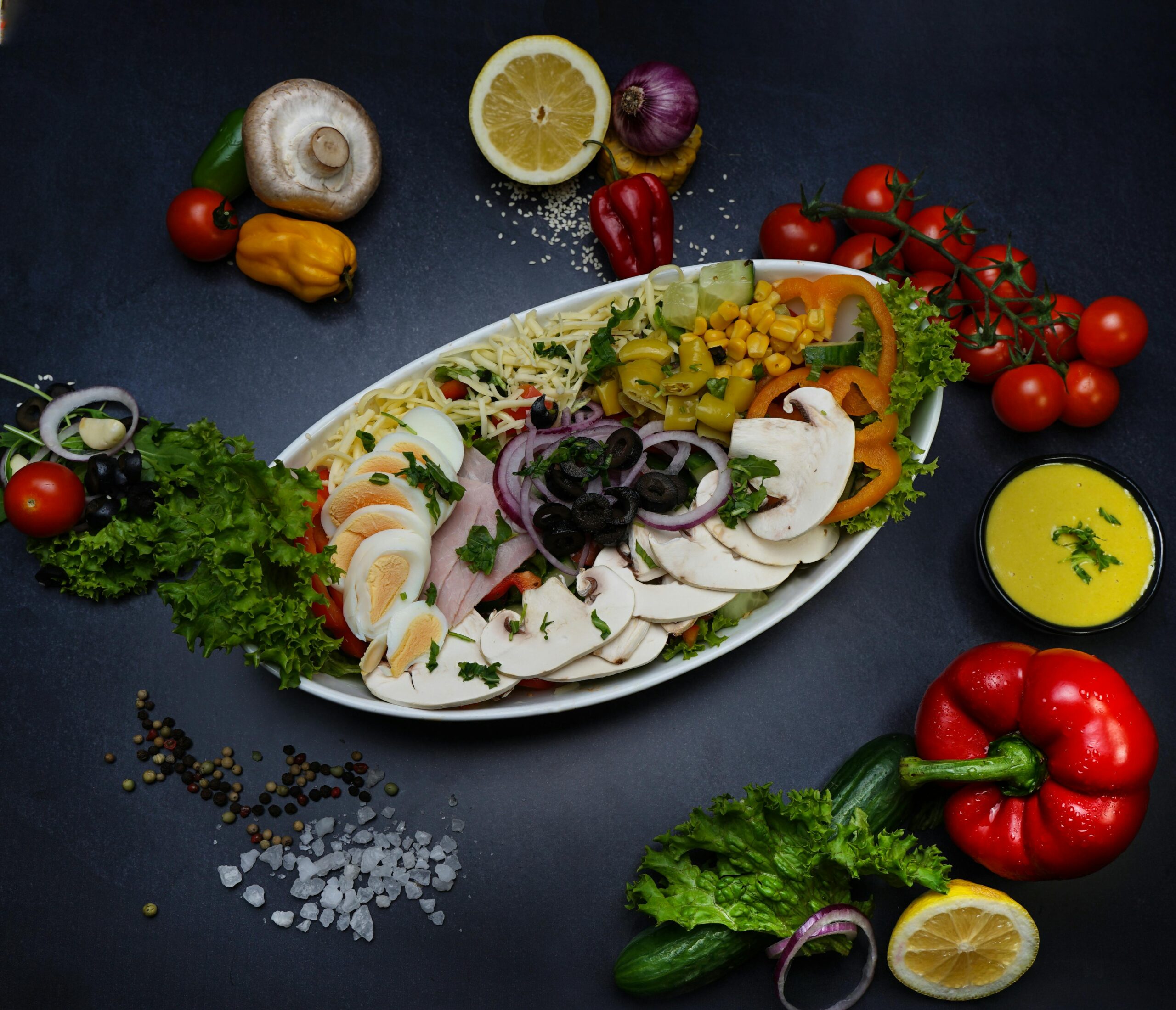 Lebendiger Gartensalat mit gemischtem Gemüse, Eiern und Dressing auf dunklem Hintergrund.