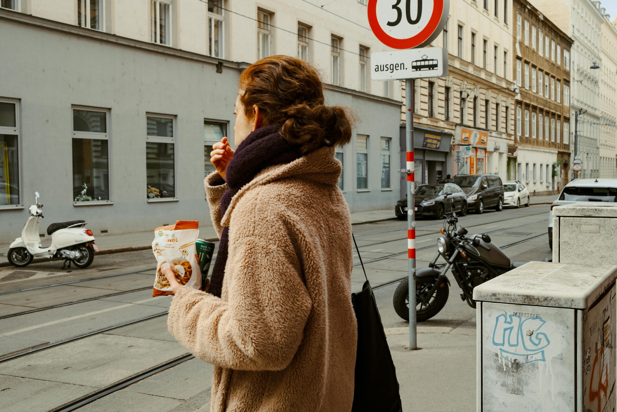 Eine Frau genießt Snacks und Kaffee, während sie durch eine europäische Stadtstraße geht und so das städtische Leben vorführt.