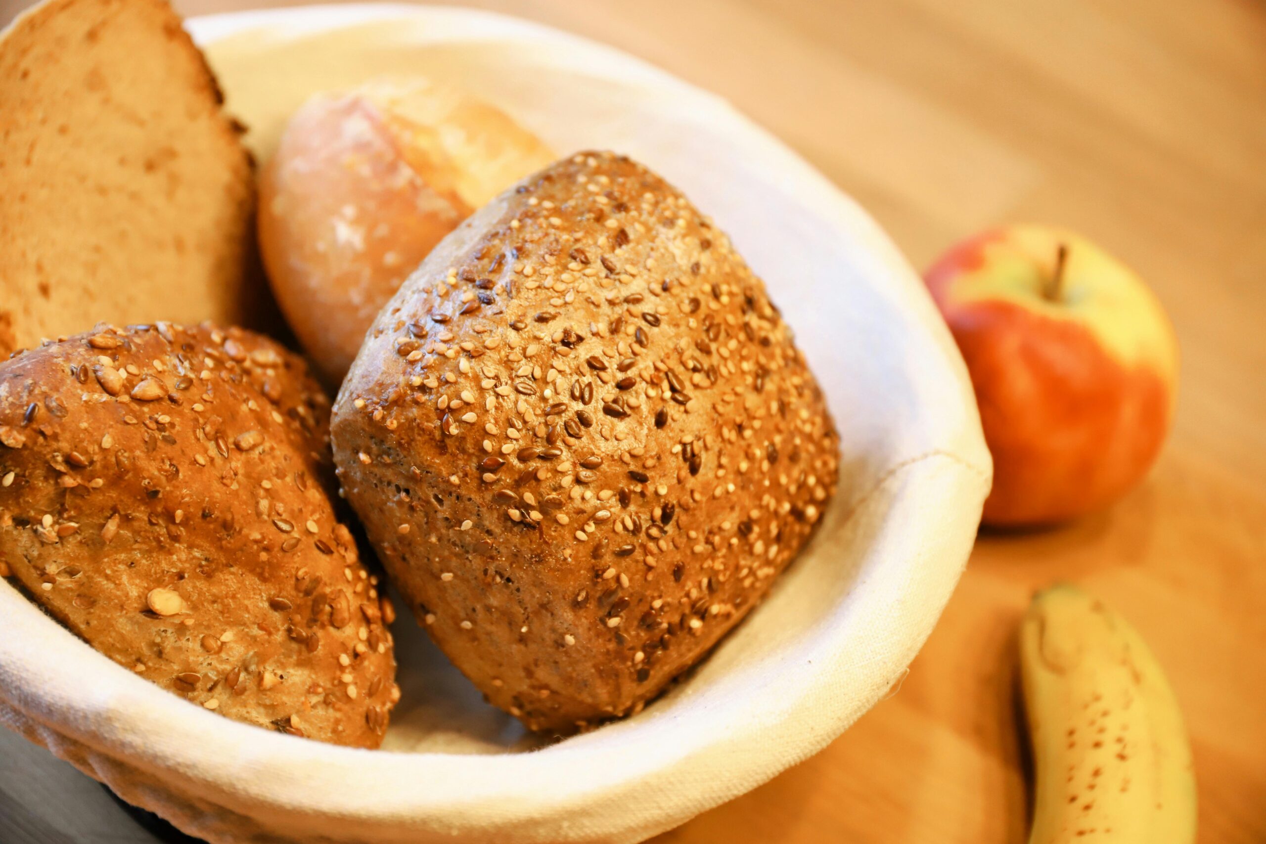 Eine Auswahl an frischen Mehrkorn- und Vollkornbrötchen, serviert in einem Korb mit Obst.